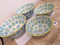 Four porcelain bowls arranged showing interior and exterior floral design featuring blue and green flowers with yellow trim on rims