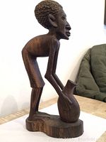 Side view of the wooden African man sculpture showing textured hair, facial profile, and pot held in hands.