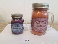 Photo of two candles: larger Blood Orange and smaller Black Raspberry Vanilla in glass jars with metal lids.