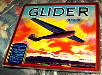 Photo of Glider Brand fruit crate advertising lithograph in Lucite frame showing vibrant image of airplane at sunset and text.