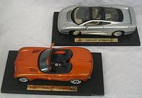 Top view of both Maisto model cars on display bases, showing Jaguar XJ220 and Dodge Concept Vehicle in orange and silver colors.