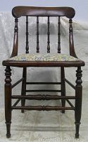 Front view of antique wooden chair showing turned spindles on backrest and needlepoint seat cushion.