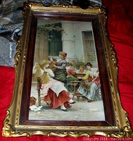 Print of Art Nouveau women in courtyard scene in ornate two-tone wooden shadow box frame with gold ornamental edges, showing entire front view.