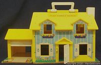 Front view of yellow and blue Fisher Price Play Family House showing roof handle, front door open, and attached garage on left.