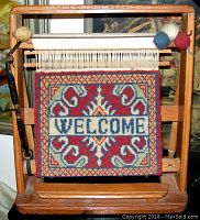 Front view of wooden display loom with colorful handwoven welcome rug mounted.