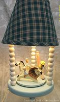 Shows the front view of the musical merry-go-round lamp with plaid fabric shade, light blue base, and rotating animal figures.