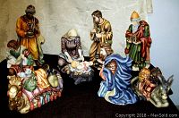 Photo displaying all eleven nativity porcelain figurines arranged on a black surface against a floral beige curtain backdrop.