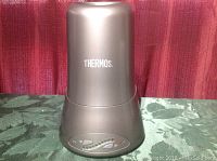 Silver Thermos wine chiller unit with control buttons and LED indicators on the base, placed on a green tablecloth with red background.