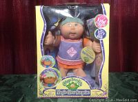 Front view of Cabbage Patch Kids Magic Glow Surprise doll Makena Daphne packaging, doll visible inside box with colorful graphics and labels.