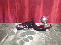 Side view of black metal trailer hitch with a 2 inch chrome-plated hitch ball attached and a metal locking pin in place.