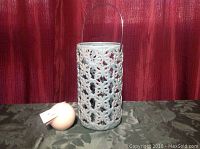 Aqua butterfly lantern placed on a surface next to an unopened round candle, seen against a red background.