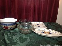 Lot of various bowls and serving trays on table with dark green tablecloth and red curtain background.