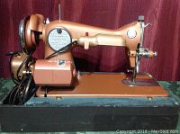 Side view of the brownish-orange Fleetwood deluxe sewing machine showing motor and power cord on black base.