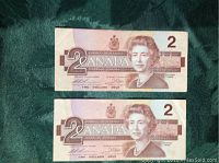 Two Canadian two dollar bills displayed front side up showing Queen Elizabeth II portraits, brown coloring, dated 1986