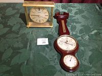Wooden barometer with attached thermometer and hygrometer, alongside Bulova table clock in gold-tone frame on green cloth.