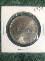Reverse side of the 1977 Canadian silver dollar coin showing the canoe design with two figures and inscriptions.