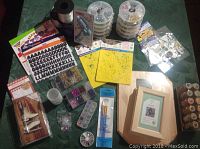 Photo of craft supplies including wooden boxes, stickers, stencils, glue gun, beads, glitter, paint brushes, and memo book arranged on a green table.