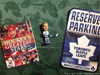 Photo showing all items together: Wendell Clark bobblehead, Toronto Maple Leafs reserve parking sign, and 'Hockey's Greatest Stars' book.