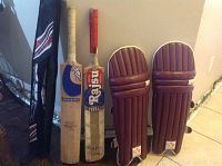 Photo showing two cricket bats, one Kookaburra and one Rajsu Yuvraj, alongside maroon cricket batting pads. Items show use wear.