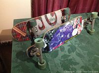 Two skateboards side by side, showing tartan plaid and graphic designs on undersides and green wheels.