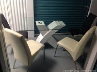 Front view of glass dining table with white X-shaped base and four chairs