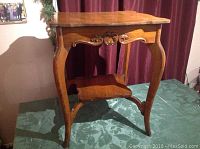 Front angled view of the vintage hardwood two-tier table showing carved apron and legs.