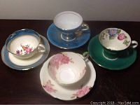 Top view of four Aynsley teacups and matching saucers in blue, green, cream, and white with floral patterns and gold accents.