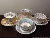 Four Paragon England teacups displayed with matching saucers, showing different floral and gold designs