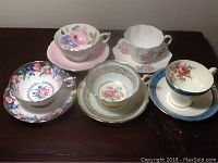 Top view group photo of five English porcelain teacups and saucers, showing various floral designs and gold accent details