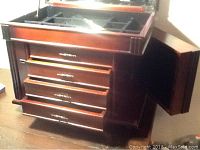 Wood jewelry chest with four front drawers, a lift top, and side panels opened to show hooks for necklaces.
