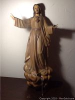 Front view of tall hand carved wooden statue of Jesus on clouds, showing open arms and detailed robes with painted accents.