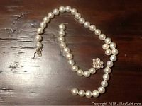Full length view of the pearl necklace showing the round white pearls and the 14k gold decorative clasp.