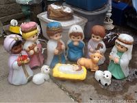 Photo of ten-piece Precious Moments style nativity set including Mary, Joseph, Baby Jesus, three Wise Men, shepherd, and sheep figurines arranged on outdoor surface