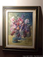 Framed oil painting showing a bouquet of flowers in a glass vase, small blue box, and metallic pitcher on a surface, with vintage frame.