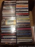 Top view showing multiple stacks of CD jewel cases in a box, displaying a variety of album spine titles