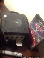 Nintendo GameCube console shown with the disc case for the game Cars beside it, power and AV cables visible.