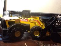 Side view of Tonka Mighty Loader toy showing yellow body with black plastic wheels and scoop bucket, model number and logo decals visible.