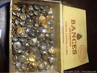 Overview photo showing a box filled with a large quantity of mixed metal uniform buttons in silver and gold tones.