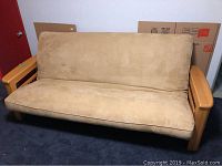 Full view of beige futon sofa with wooden armrests on a dark carpet