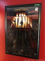 Framed full view of The Stand movie poster against a red wall, showing poster text and silhouetted figure.