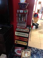Wide angle photo showing the popcorn maker on top of the themed wooden stand with vintage cinema signage around it and some additional coffee decor signs below.