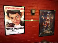 Wide shot showing both framed posters mounted on a red brick wall, Ferris Bueller's Day Off on left, Christmas Vacation on right.