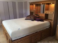 Full view of California king captain bed with mattress and pillows on top, showing headboard with cubbies, drawers, mirror, and lights.