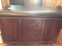 Front view of wooden Lane record storage bench with padded black seat, two brass-handled drawers and keyhole lock.