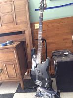 Full-length view of the black Silvertone bass guitar on a stand next to wooden furniture.