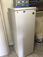 White upright freezer closed, showing full unit from left angle.