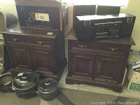Pair of dark wooden end tables with ornate brass handles, one drawer, and cabinet doors shown together with household items around them.