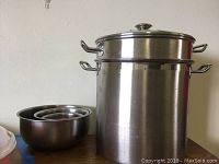 Tamale steamer pot and three nesting metal mixing bowls on table against wall.