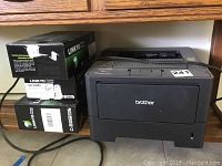 Brother HL-54700DW laser printer placed on shelf next to three stacked boxes of LINKYO cartridges