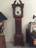 Full view of the grandfather clock showing entire height, wooden case, and glass front with clock face visible.